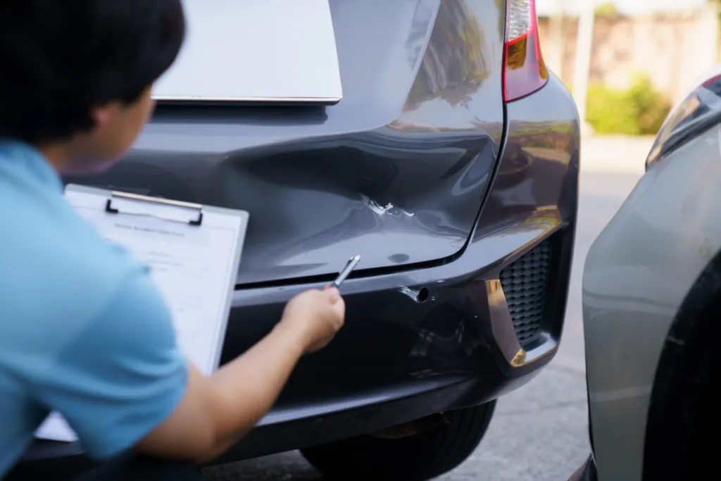 Person documenting rear bumper damage after a rear-end car collision